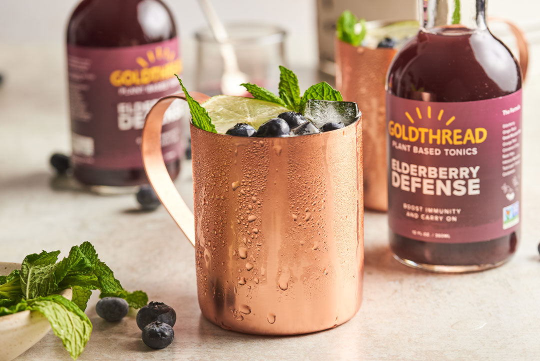 Goldthread Plant-Based Tonics Elderberry Mule in a copper mug garnished with mint, lemon, and blueberries