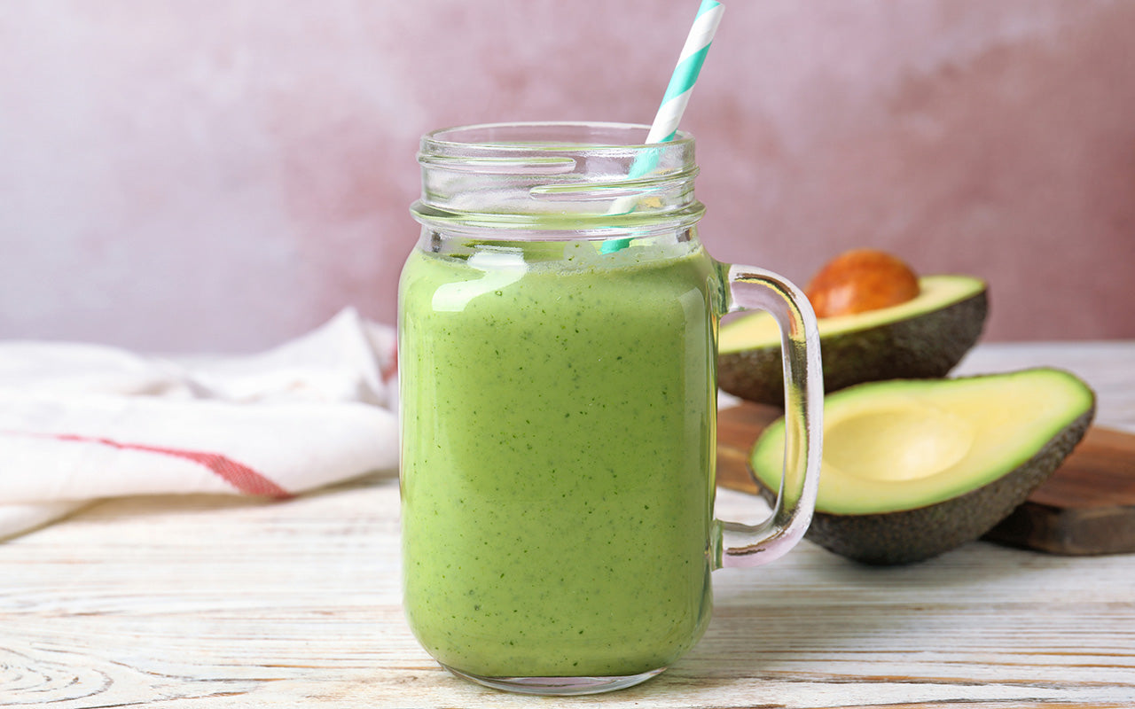 Green avocado smoothie in a mason jar with a blue striped straw with a halved avocado in the background