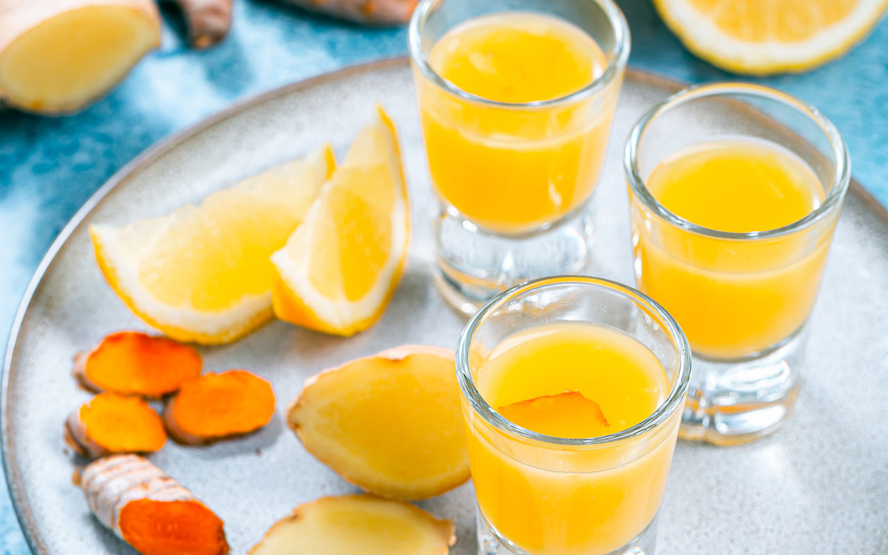 Turmeric Ginger Shots on a light blue ceramic plate surrounded by chopped turmeric, ginger, and lemon pieces