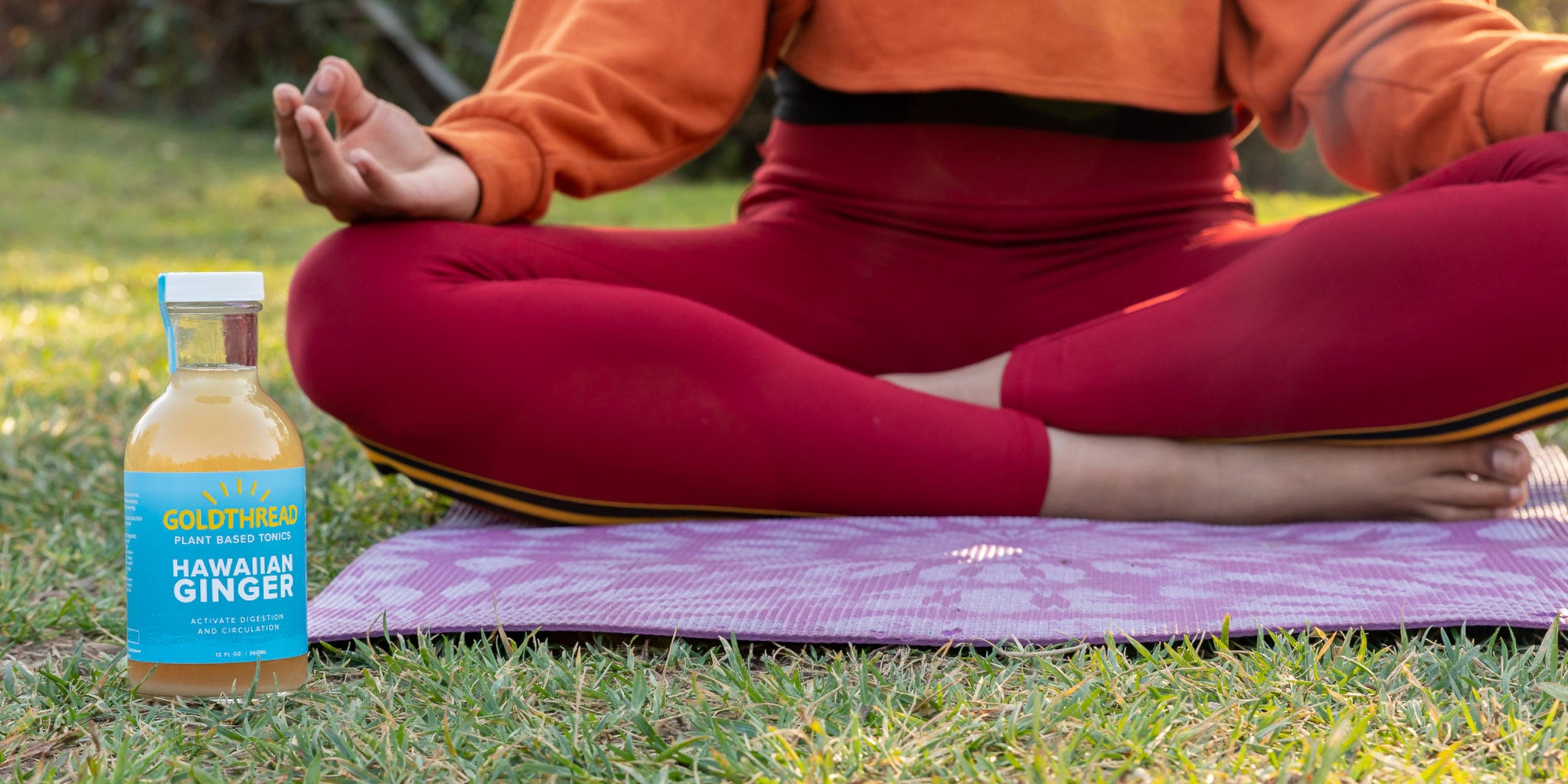 A woman with curly hair and glasses relaxes on an orange rug, leaning against a sofa. She's typing on a laptop, creating the perfect atmosphere for nurturing both creativity and immunity with the help of Goldthread tonics.