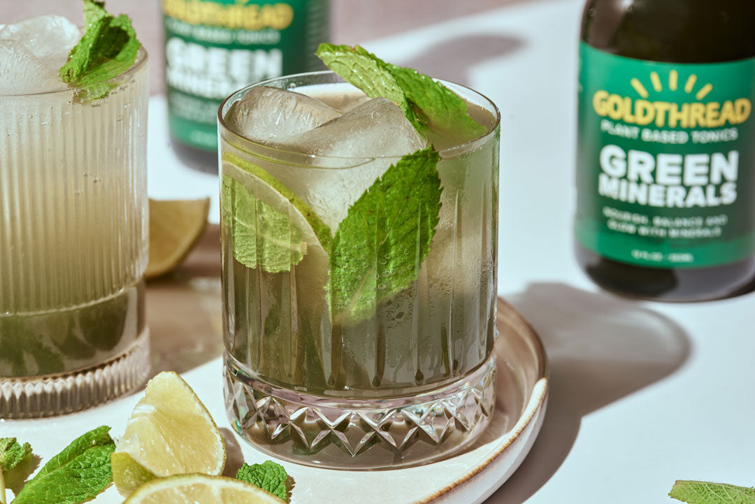 Goldthread Plant-Based Tonics Minty No-Jito Mojito Mocktail served in a rocks glass over ice and garnished with mint leaves and lime with Goldthread Plant-Based Tonics Green Minerals tonic