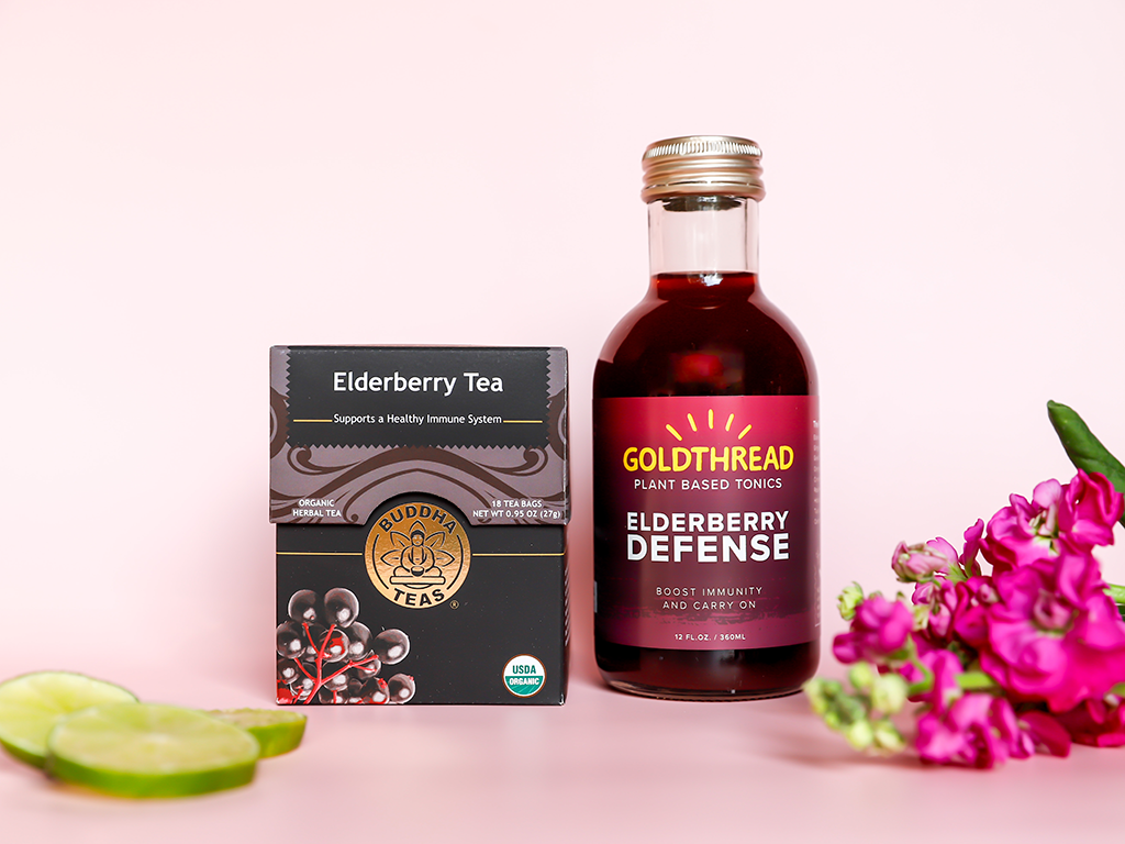 Buddha Teas Elderberry Tea and Goldthread Tonics Elderberry Defense Tonic with slices of lime and pink flowers